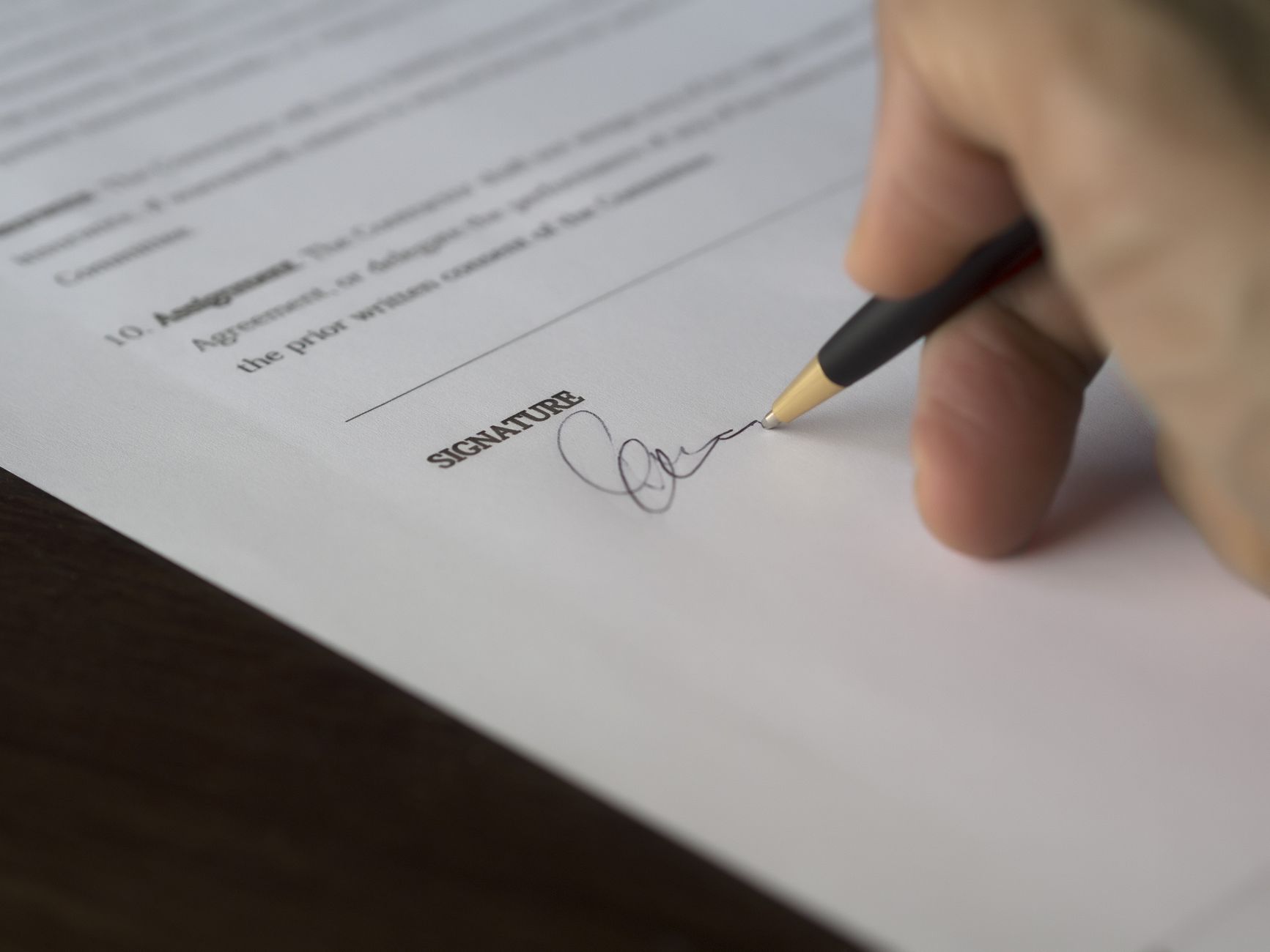 Hand unterschreibt einen Vertrag mit einem Stift auf einem Holzschreibtisch