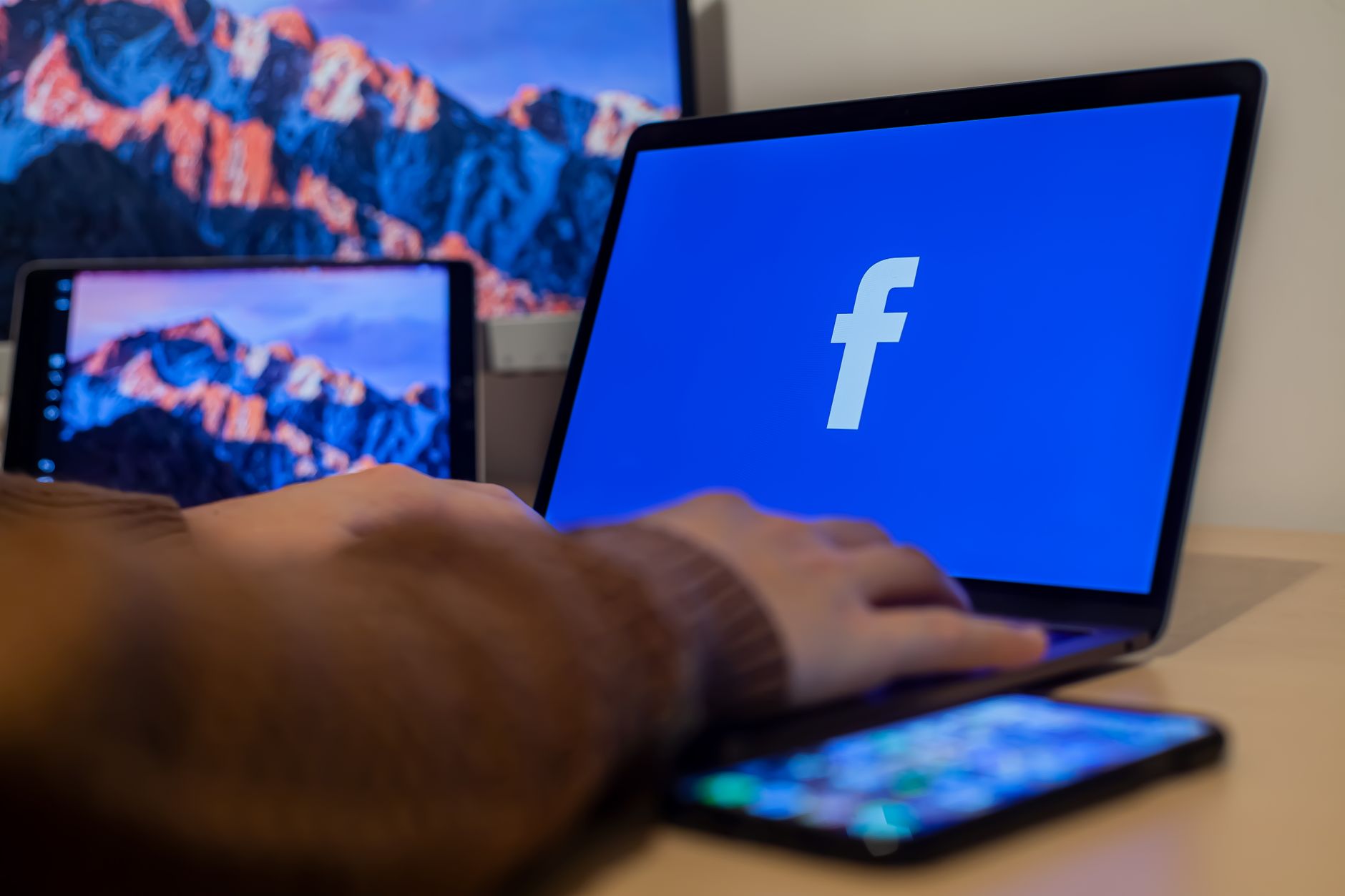 Laptop mit geöffneter Facebook-Seite an einem Arbeitsplatz mit mehreren Geräten
